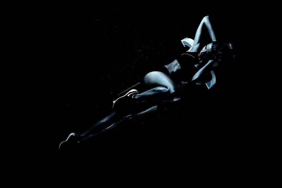 Silhouette of a woman lying on the ground mid-crunch, her form highlighted against a dark, minimalist background.