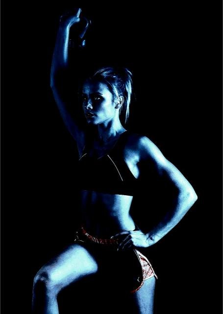 Woman in dark-toned workout gear lifting a kettlebell, illuminated by blue light, exuding strength and determination.