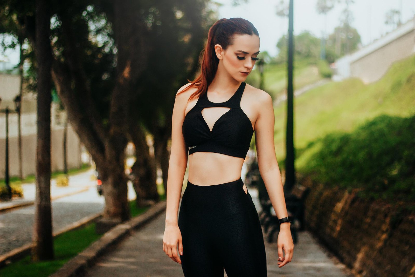 A woman in black fitness wear standing outdoors, with trees and a park path in the background, exuding confidence.