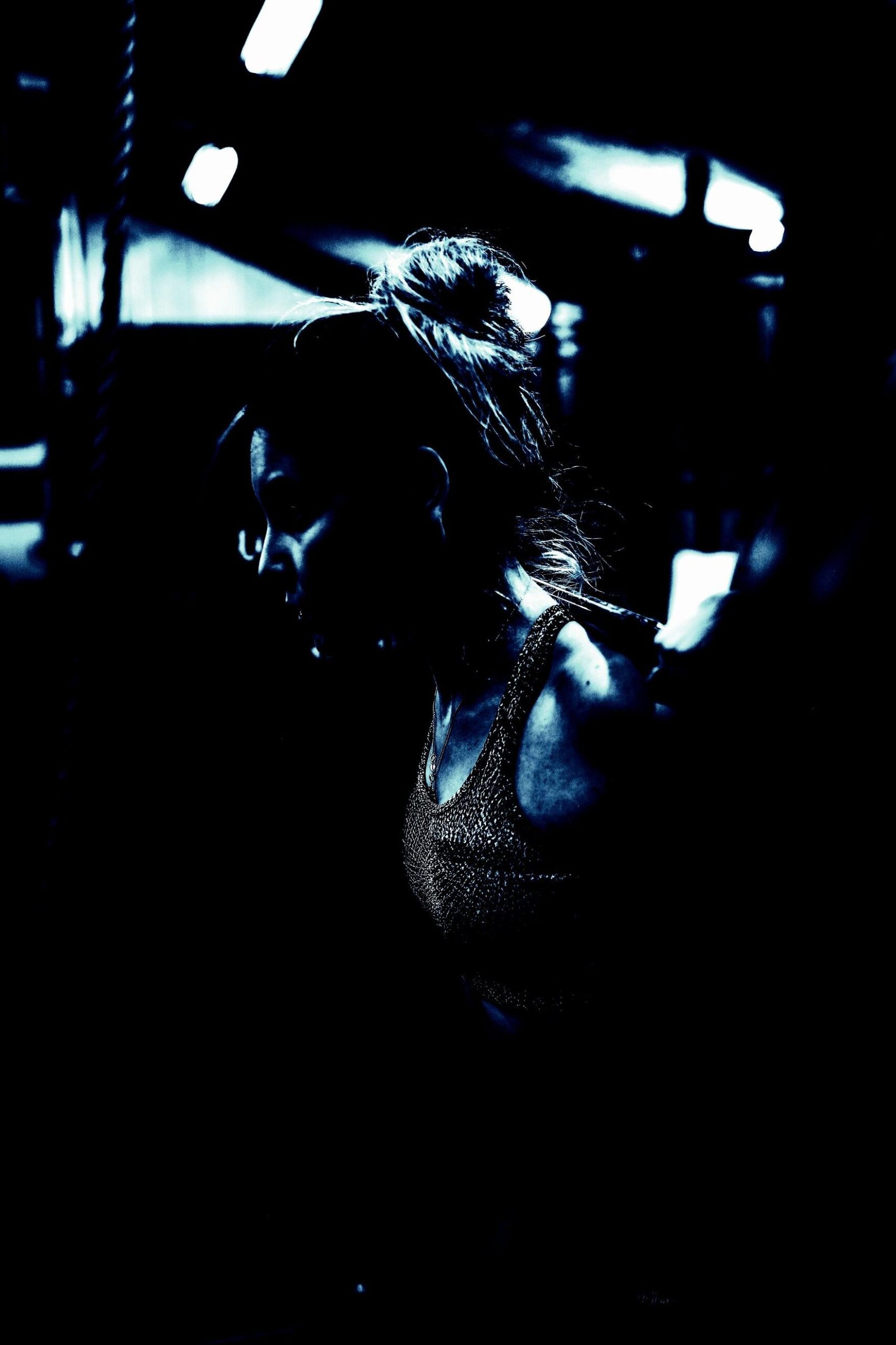 Profile view of a woman in a dimly lit gym setting, highlighting her focused expression and metallic-textured sportswear.