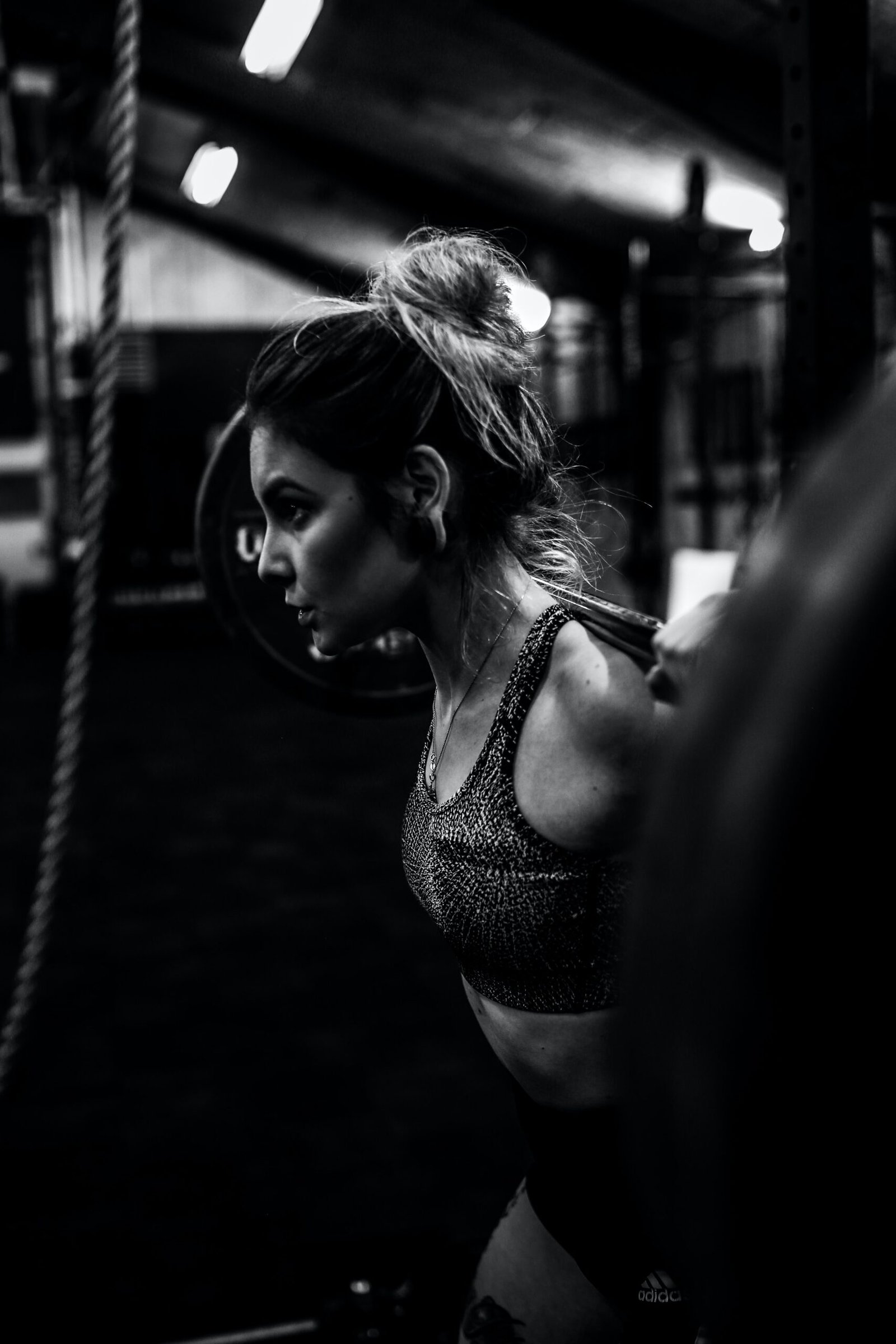 Woman lifting a barbell in a dark gym, focused and determined during her strength training session.