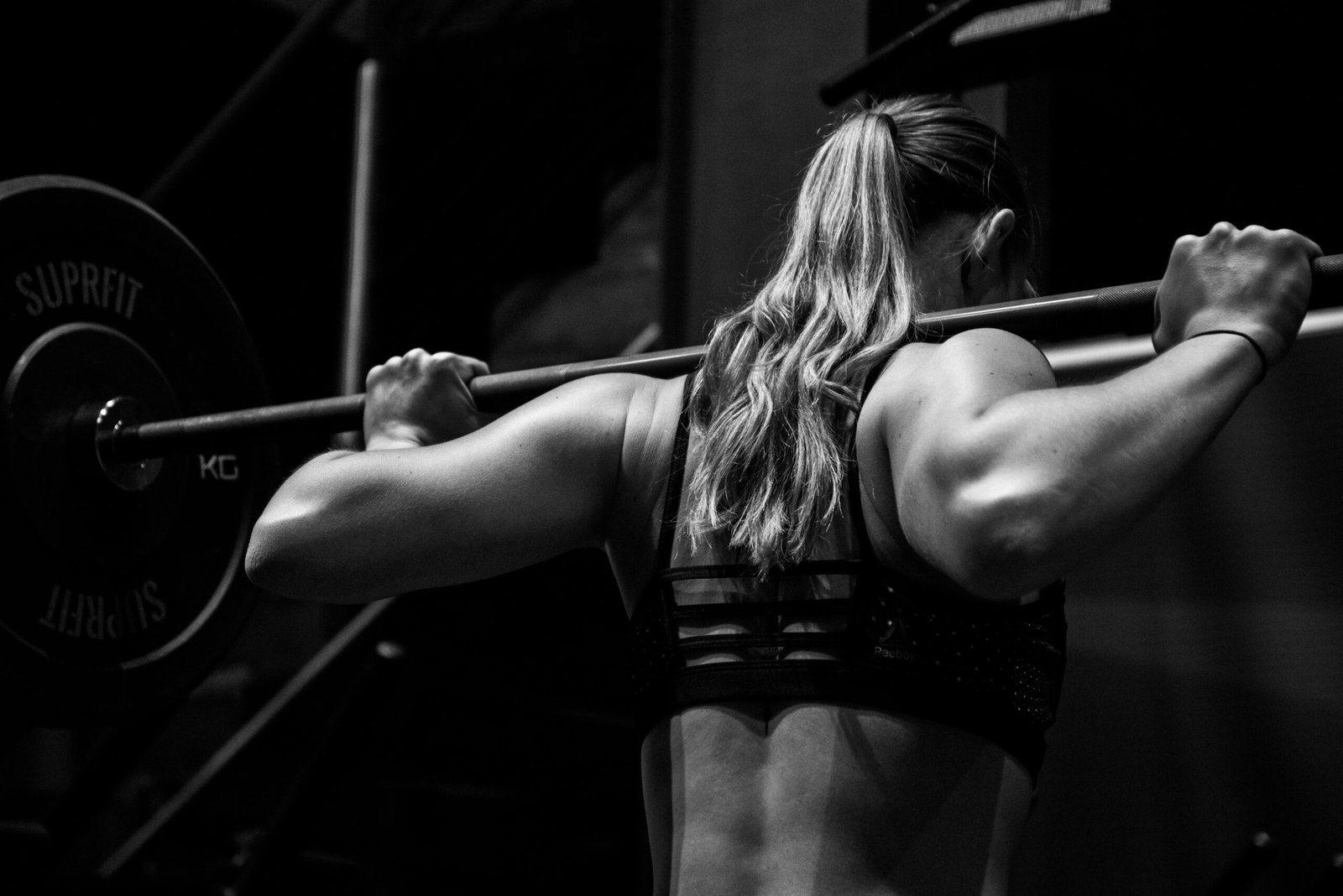 Back view of a woman performing a barbell squat, showcasing muscular definition and fitness focus.