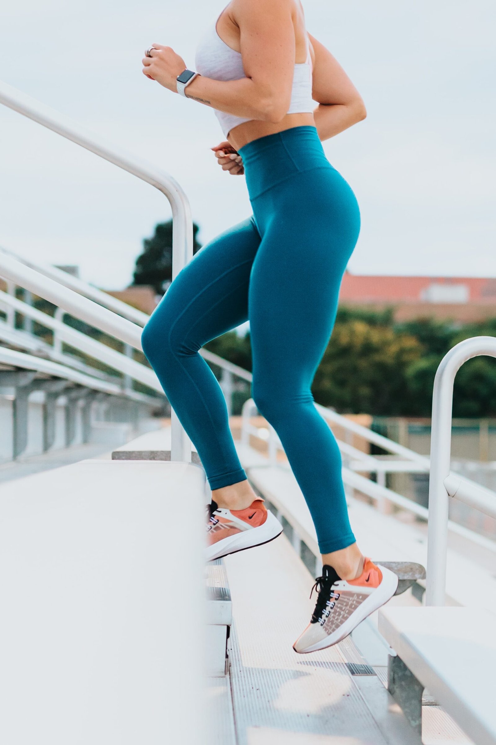 Woman running up outdoor stairs wearing blue leggings and a fitness watch, promoting an active lifestyle.
