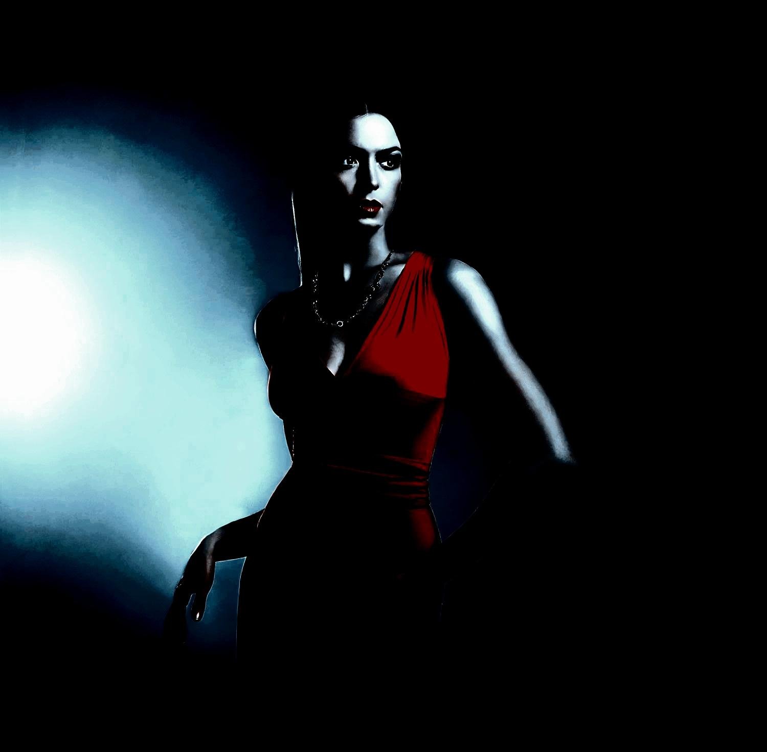 Elegant woman in a red dress standing against a moody blue-lit background, evoking gothic sophistication.