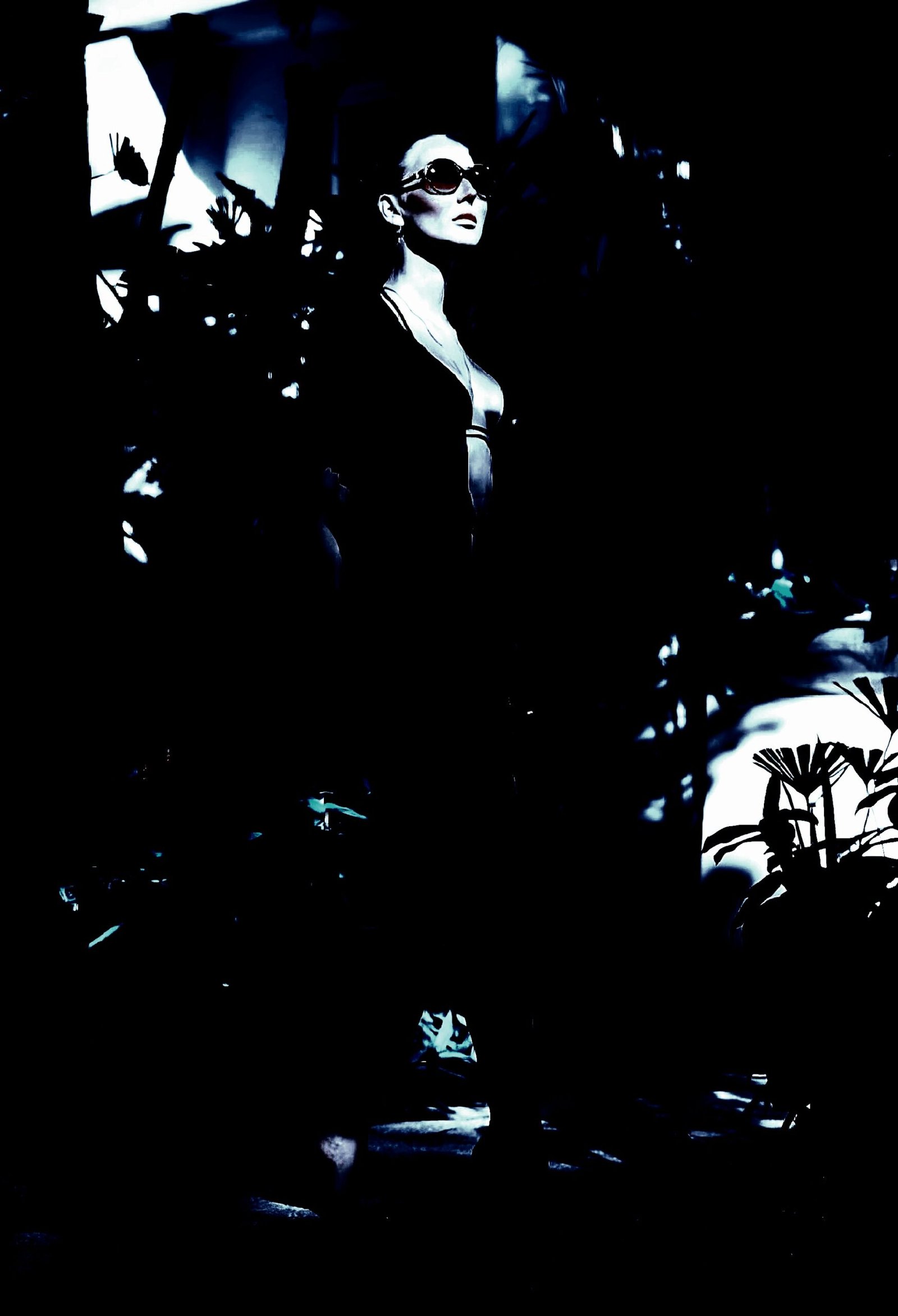 Stylish woman in sunglasses and a black dress, standing in a dark, atmospheric setting.