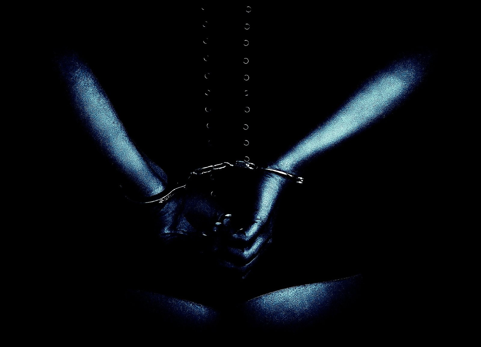 A person in a corset with hands cuffed behind their back, captured in moody, high-contrast lighting.