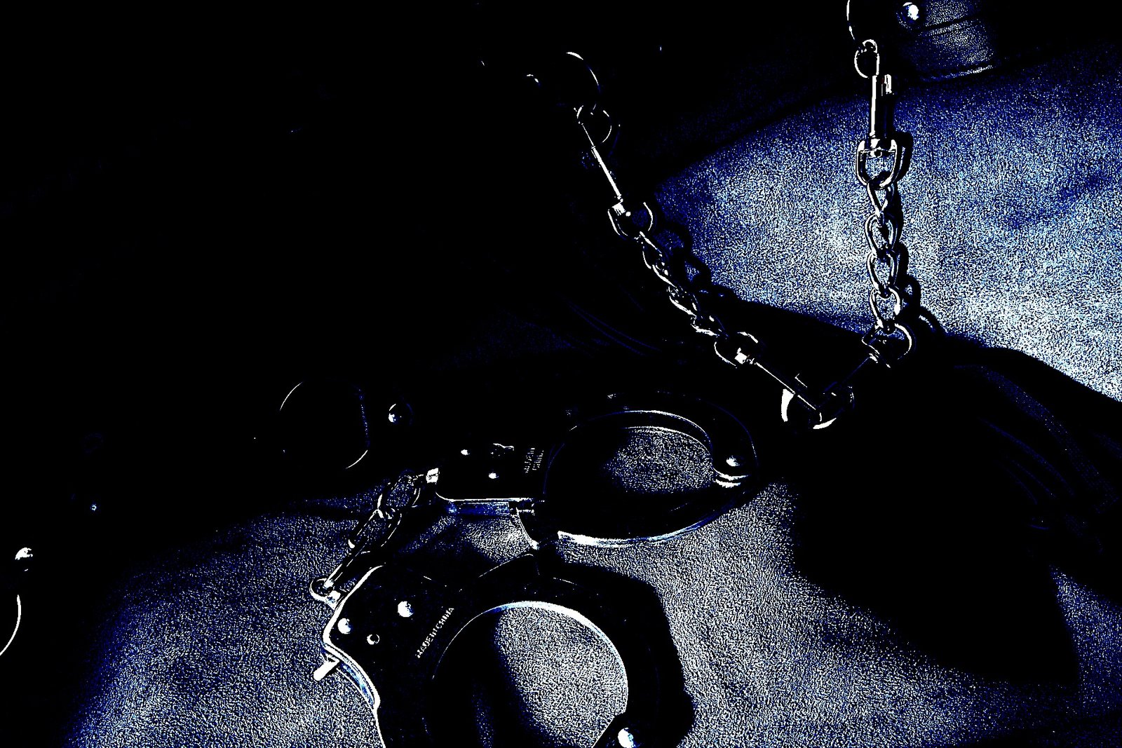 Metal handcuffs and chains laid on a dark leather surface, evoking a sense of restraint and control.