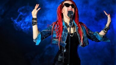 Female rock singer with red dreadlocks and dark sunglasses passionately performing against a blue smoky background.