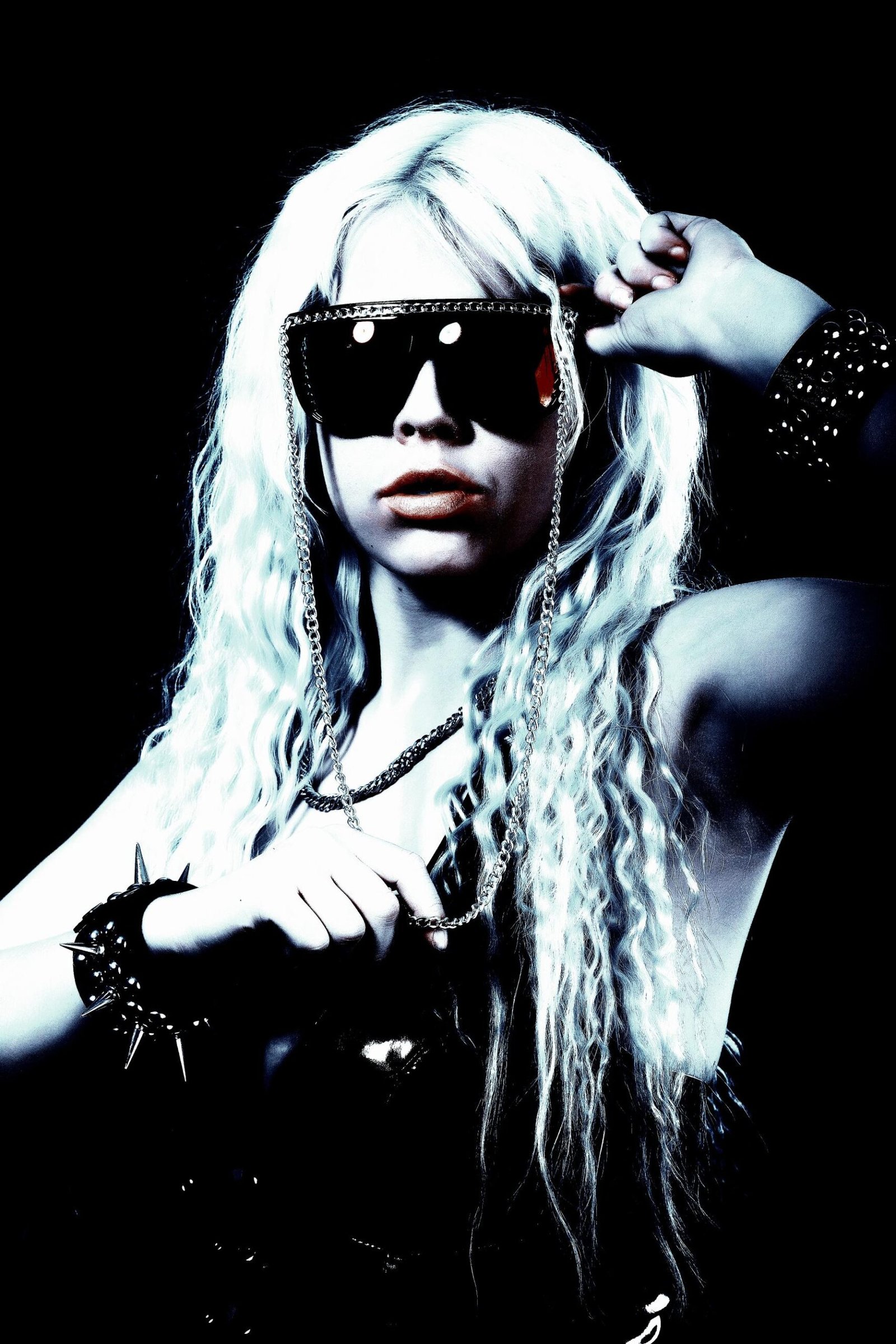 Woman with platinum blonde hair and oversized chain sunglasses, flaunting punk rock style and attitude."