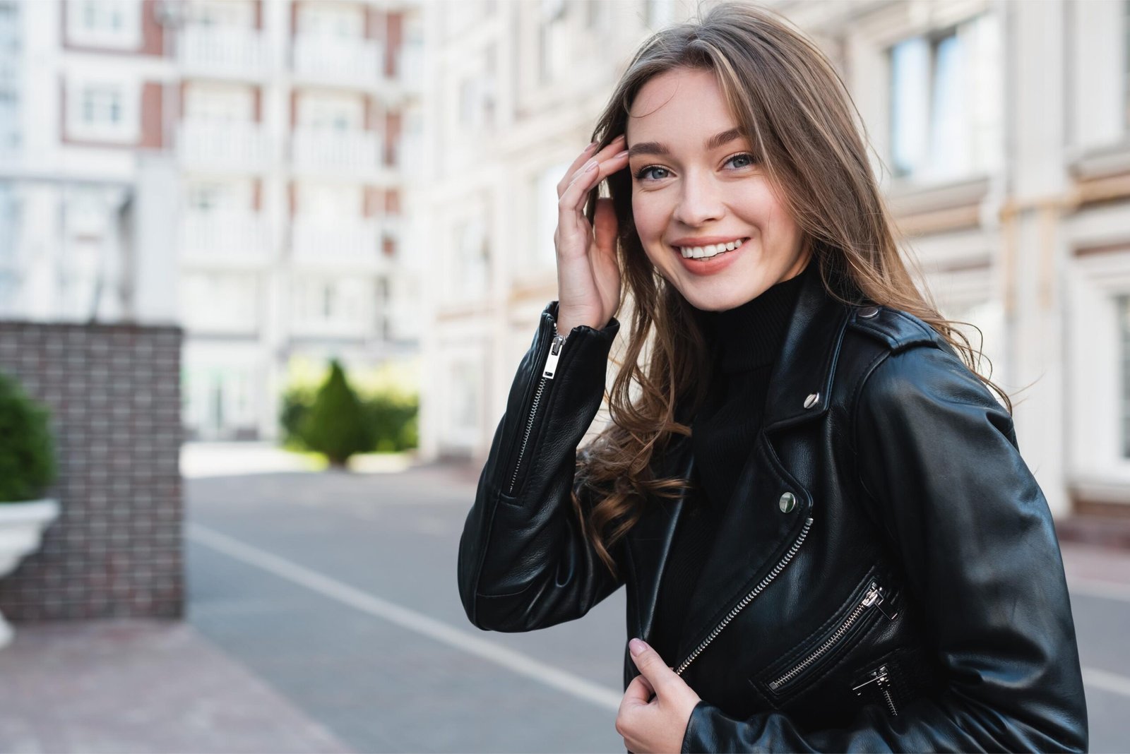 Woman in a sleek black leather jacket smiling outdoors, embodying casual goth-inspired fashion.