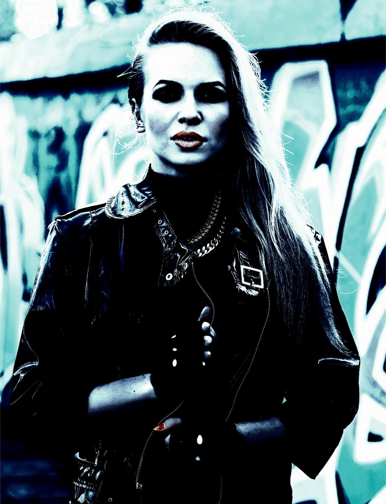 Woman in leather jacket standing confidently against a graffiti-covered wall, expressing alternative fashion.
