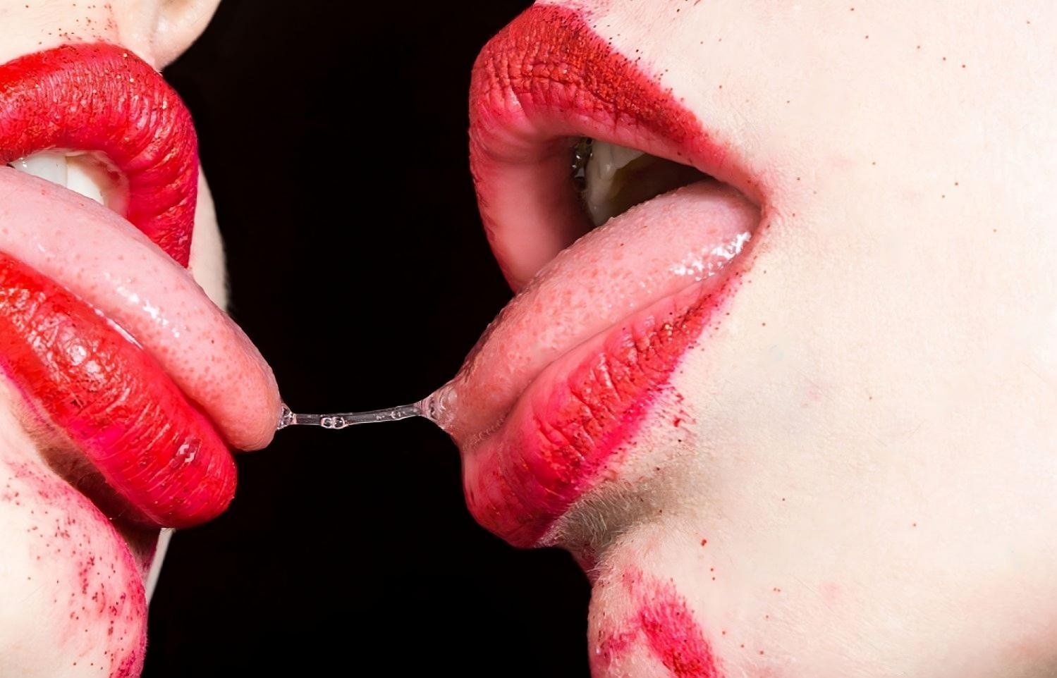 Two individuals sharing an intimate moment with bright red lips, highlighted by dramatic lighting.