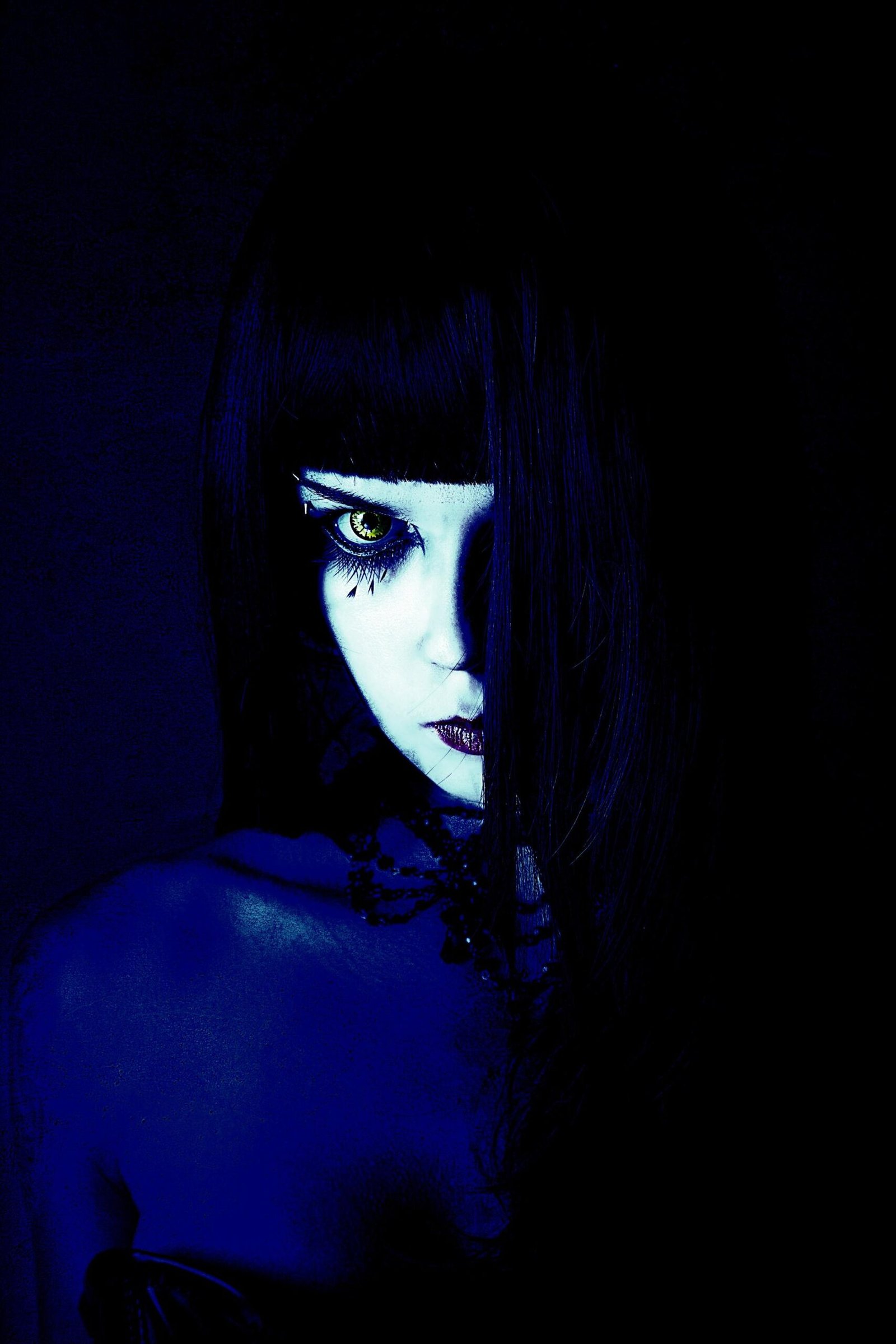Gothic woman with intense makeup and a piercing gaze, highlighted by deep shadows and mysterious lighting.
