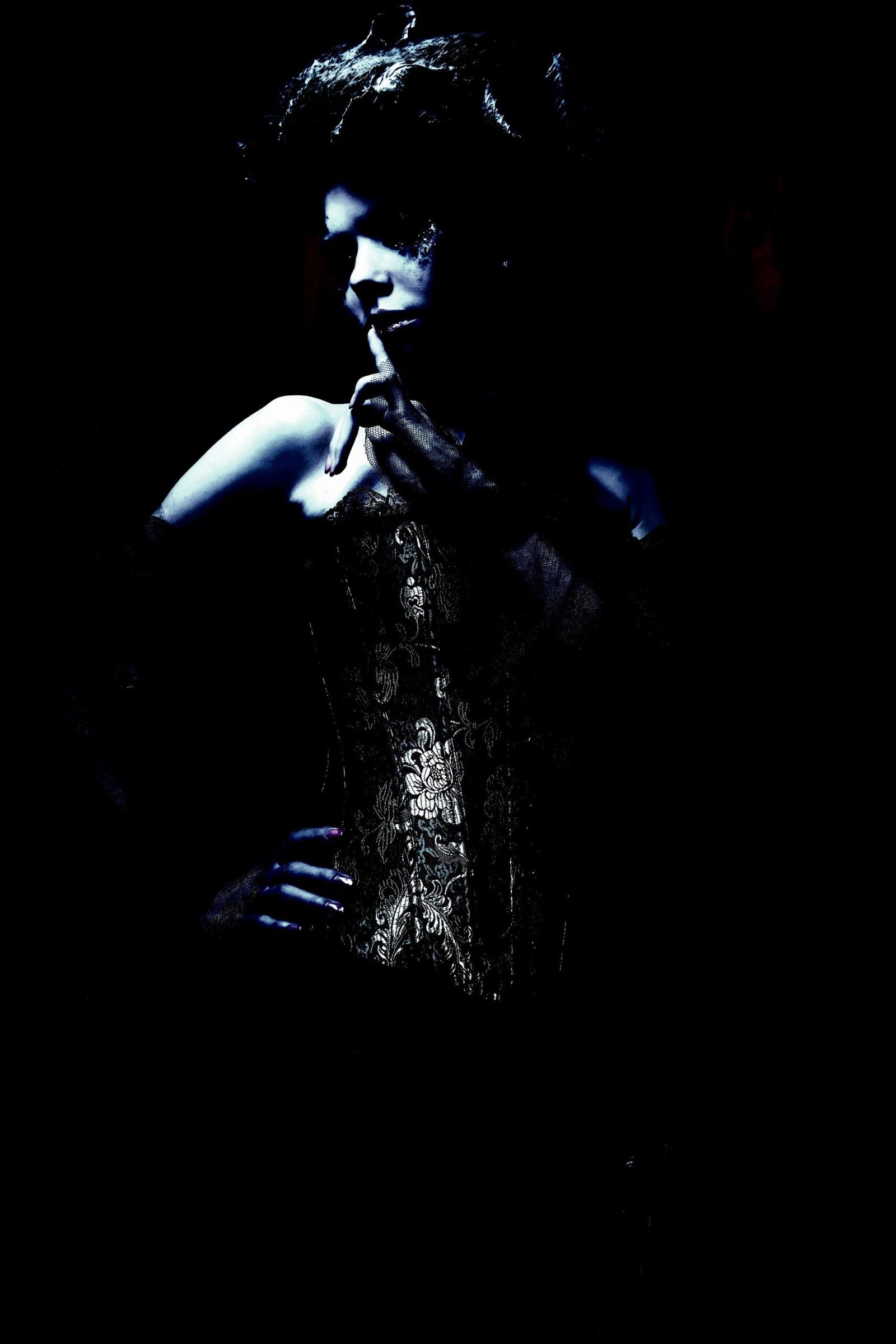 Vintage-inspired woman wearing a lace corset, striking a dramatic pose in low-key lighting.