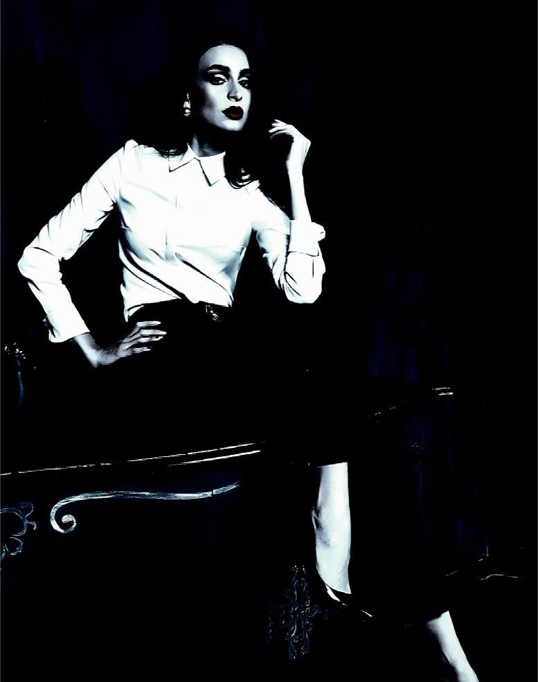 Woman in a dark room holding a book, dressed in a leather skirt and choker, with an aura of gothic allure and mystery.