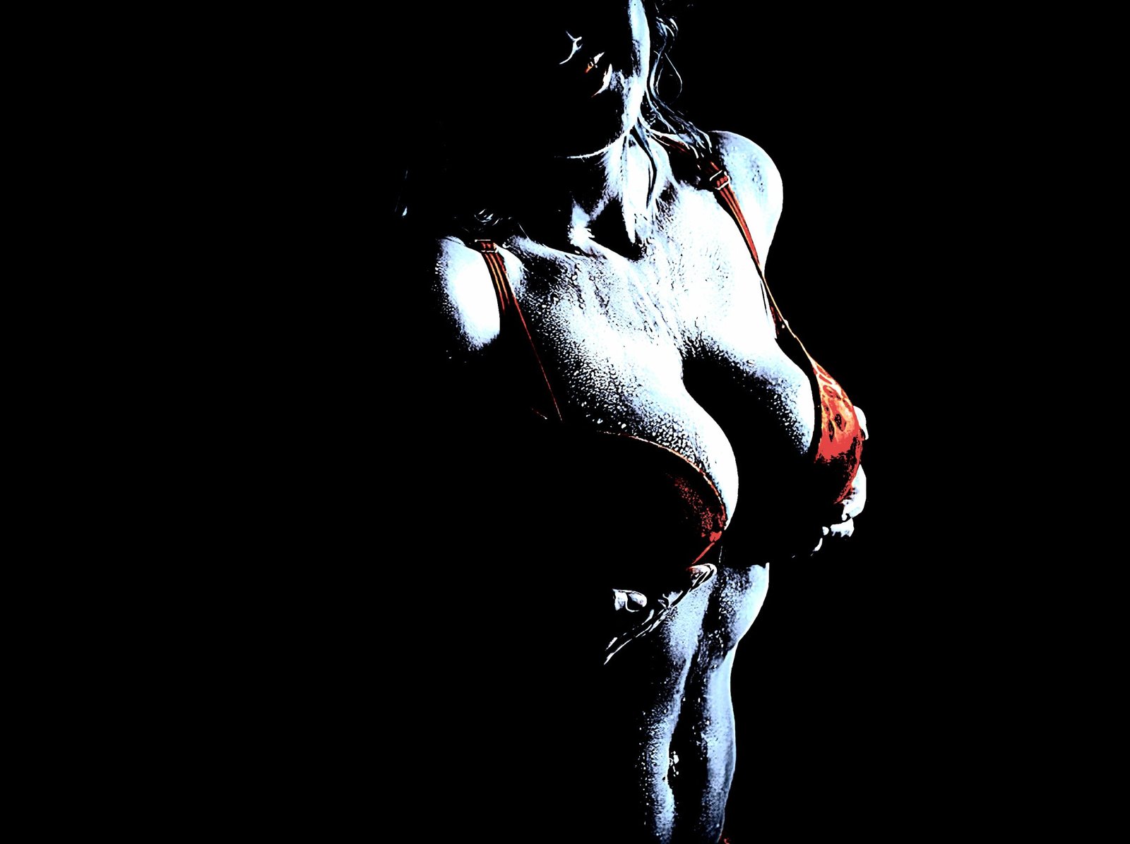 A close-up of a woman in a red bra, her torso glistening under dramatic lighting.