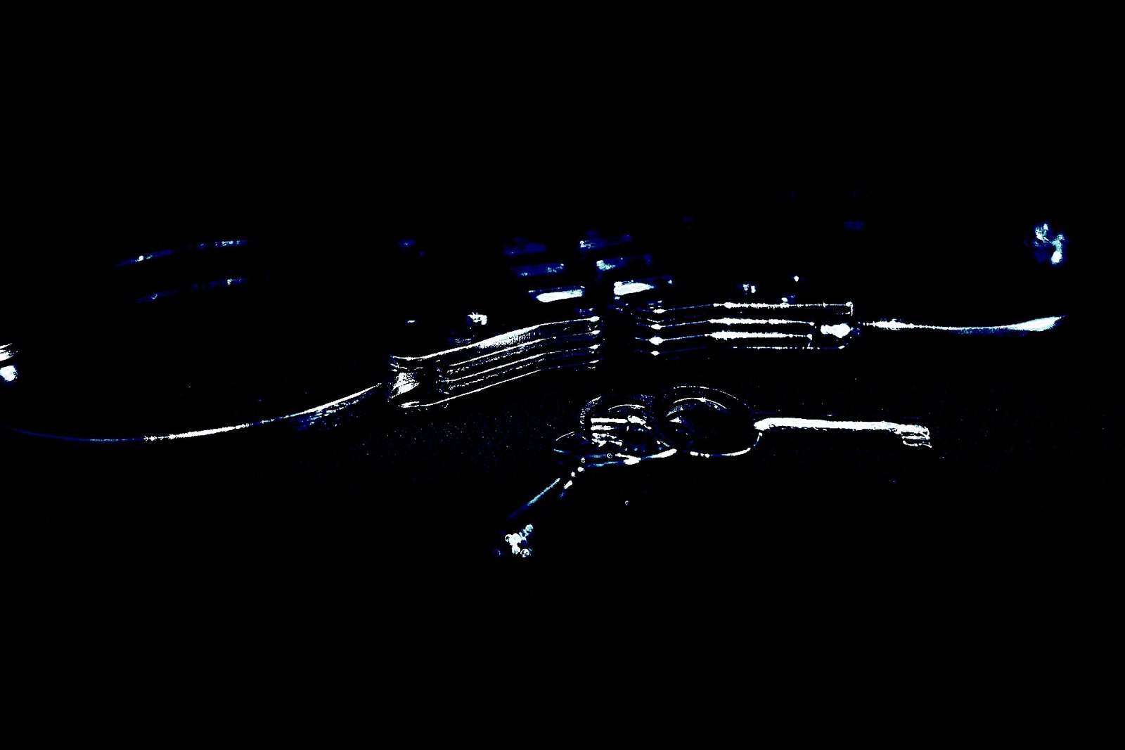 A pair of metallic handcuffs and a key on a dark surface, reflecting a dim blue light.