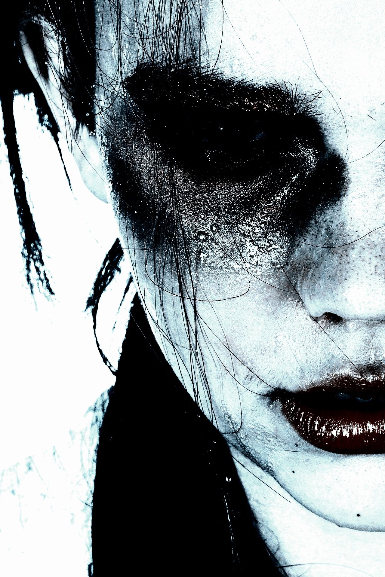 A woman's face with dark, smeared eye makeup, tangled hair, and intense expression.