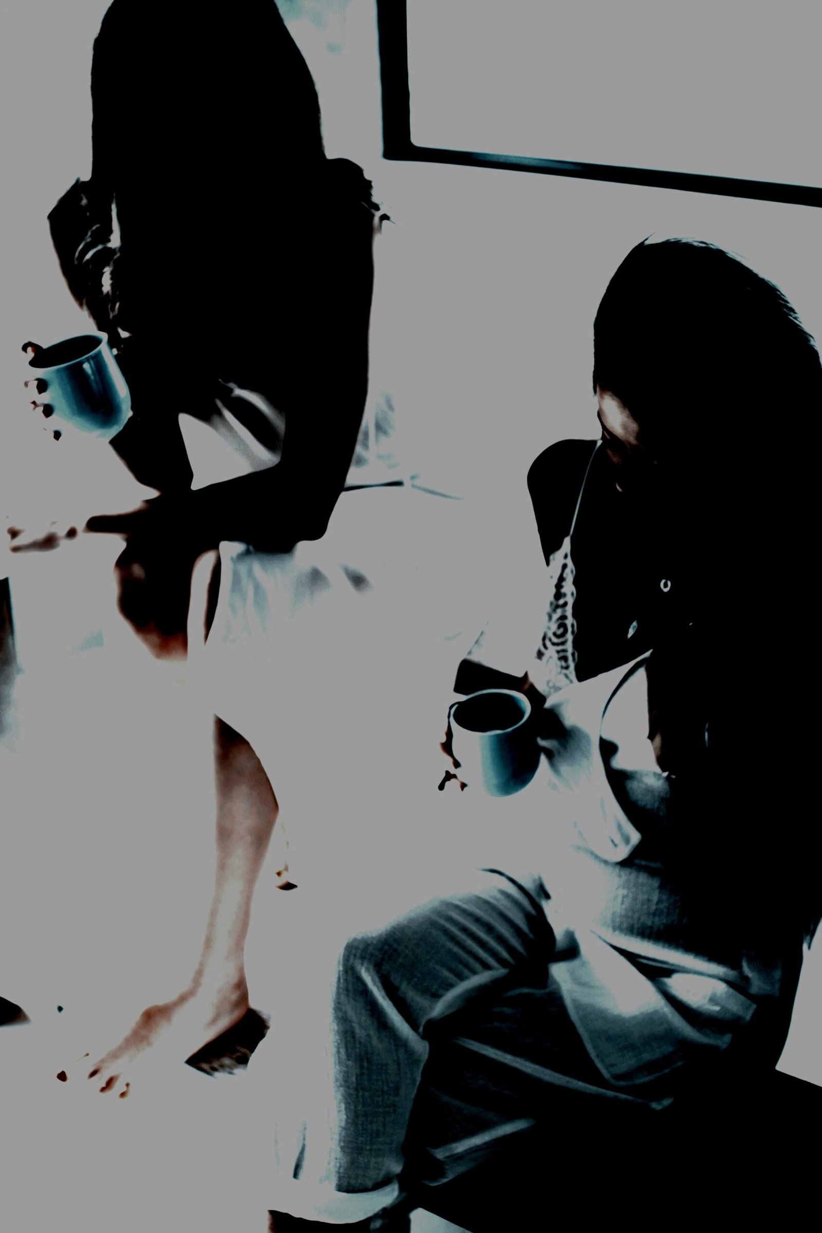 Two women in soft lighting, sitting with coffee mugs, creating a quiet, intimate atmosphere.