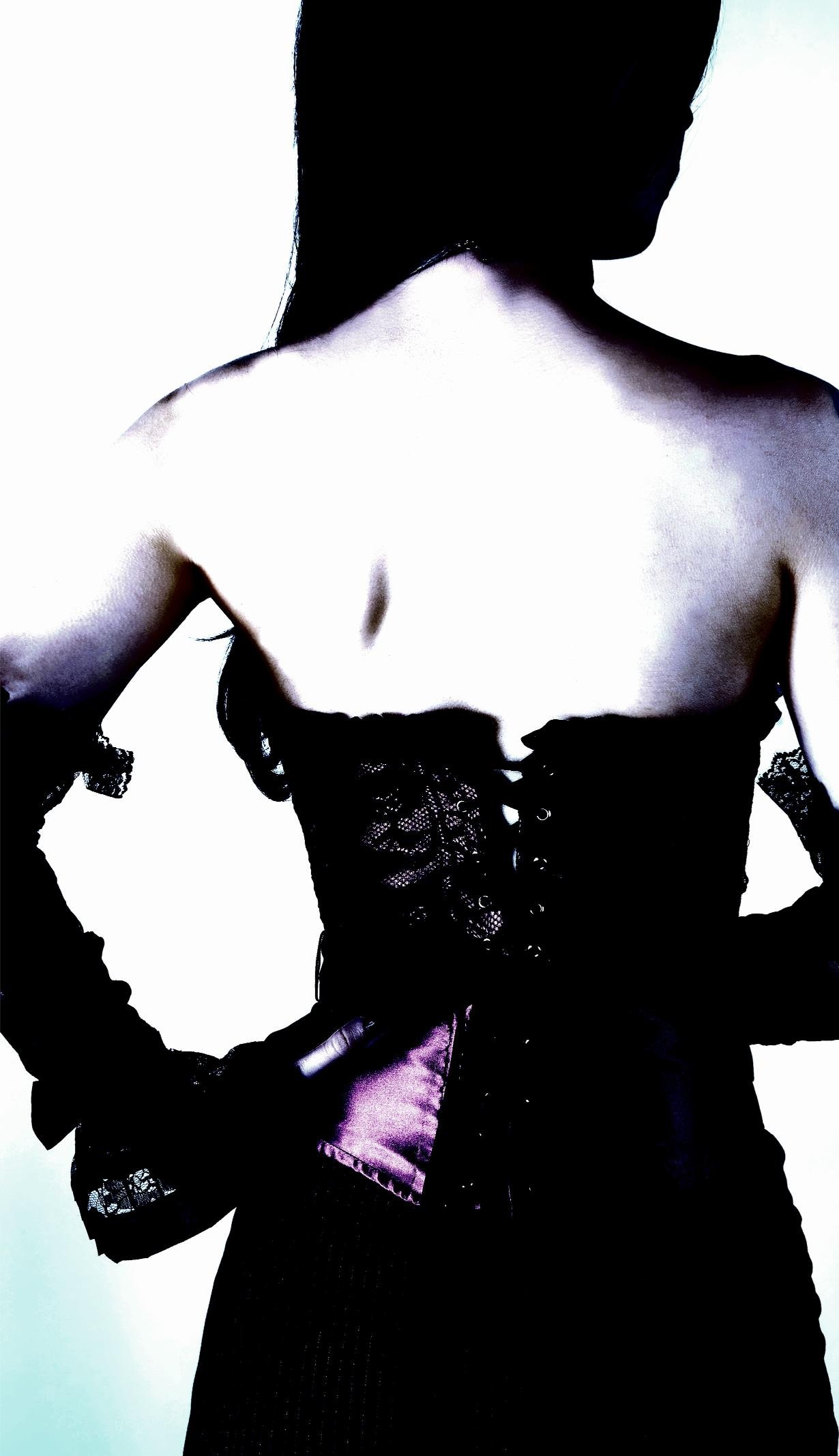 Mysterious woman in a lace corset with purple satin accents, facing away in soft lighting.