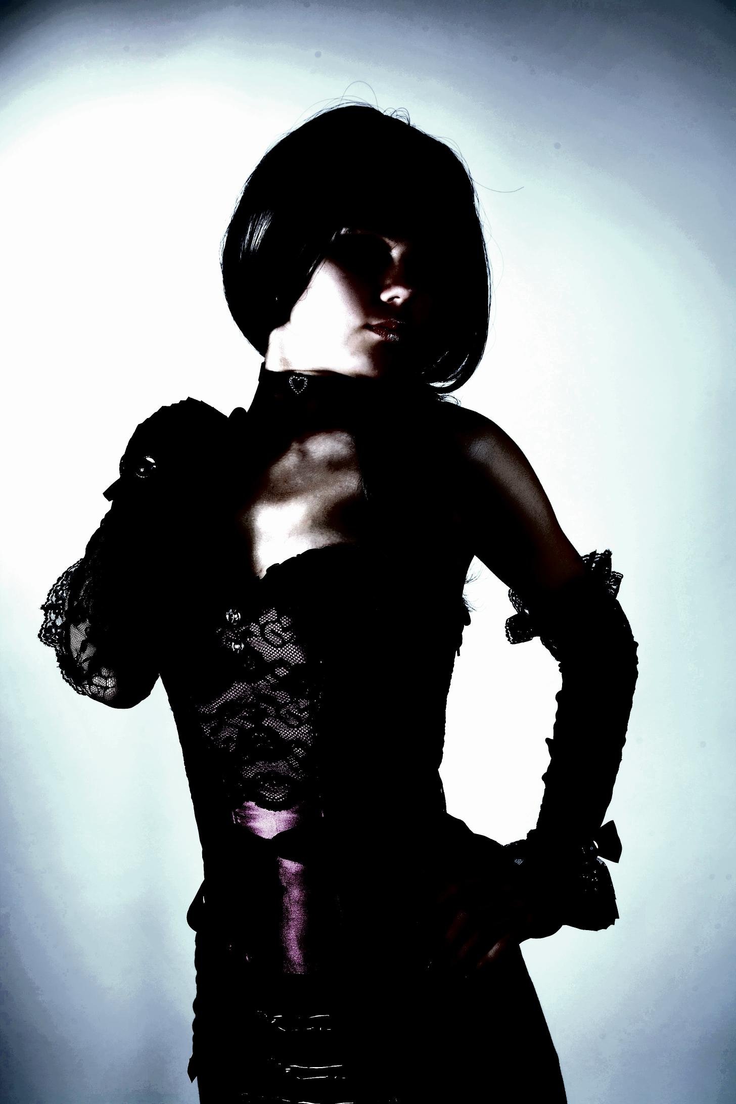 Shadowed figure in a black lace corset with purple accents, posing with dark elegance.