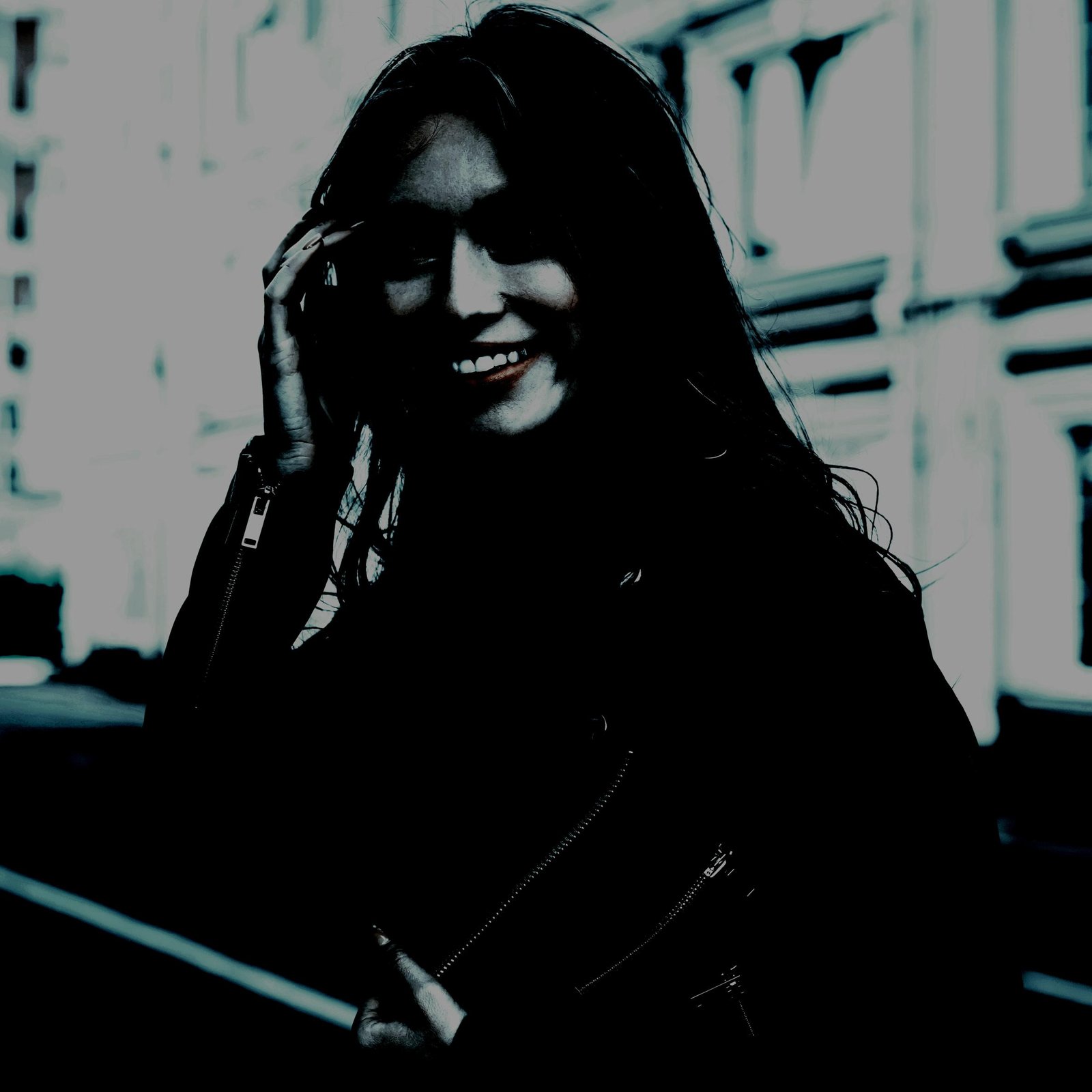 Smiling woman in a dark leather jacket, casually posing outdoors with an edgy vibe.