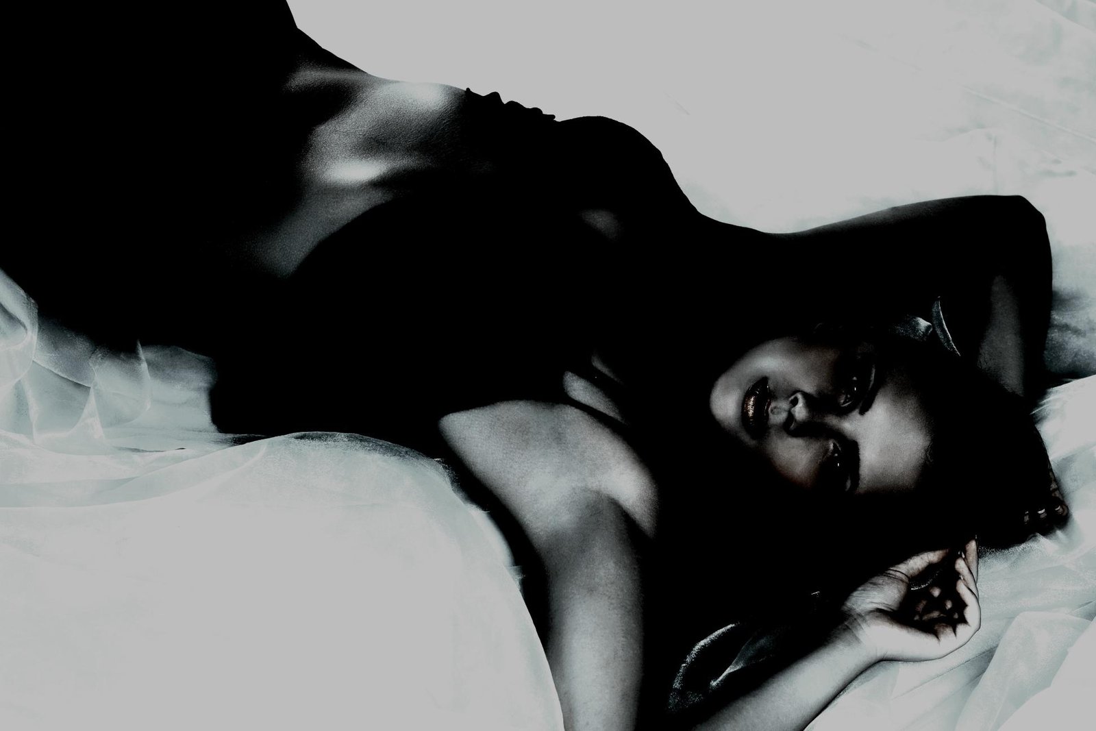 Sensual woman in a dark outfit, reclining on soft fabric with a seductive, captivating stare.
