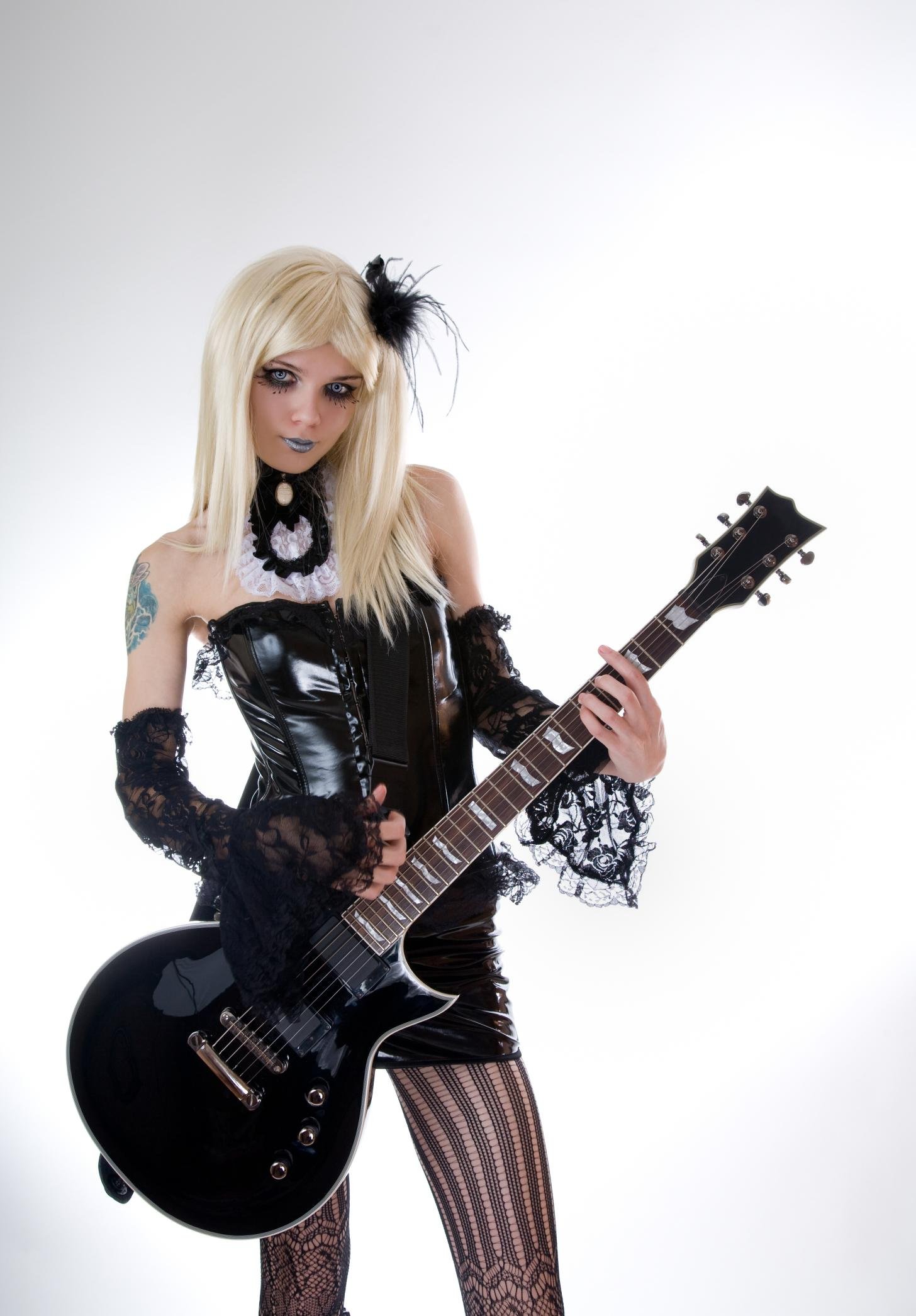 Blonde woman in gothic lace dress with black corset, holding black guitar, wearing fishnet stockings.
