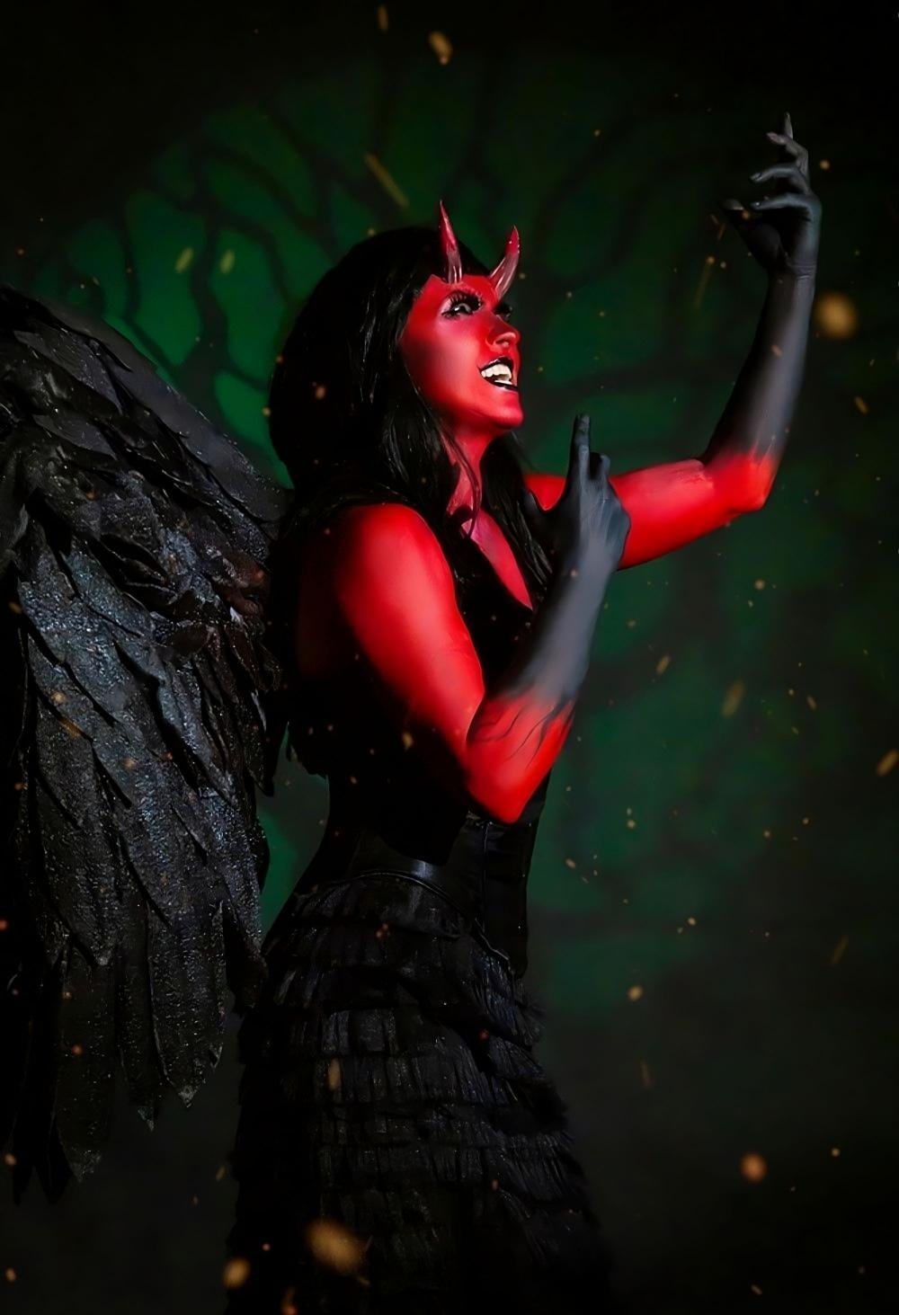 Demonic woman with red skin, black wings, and corset dress casting a spell mid-performance