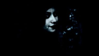 Mysterious woman with dark lipstick smirking in shadows, barely illuminated by soft light