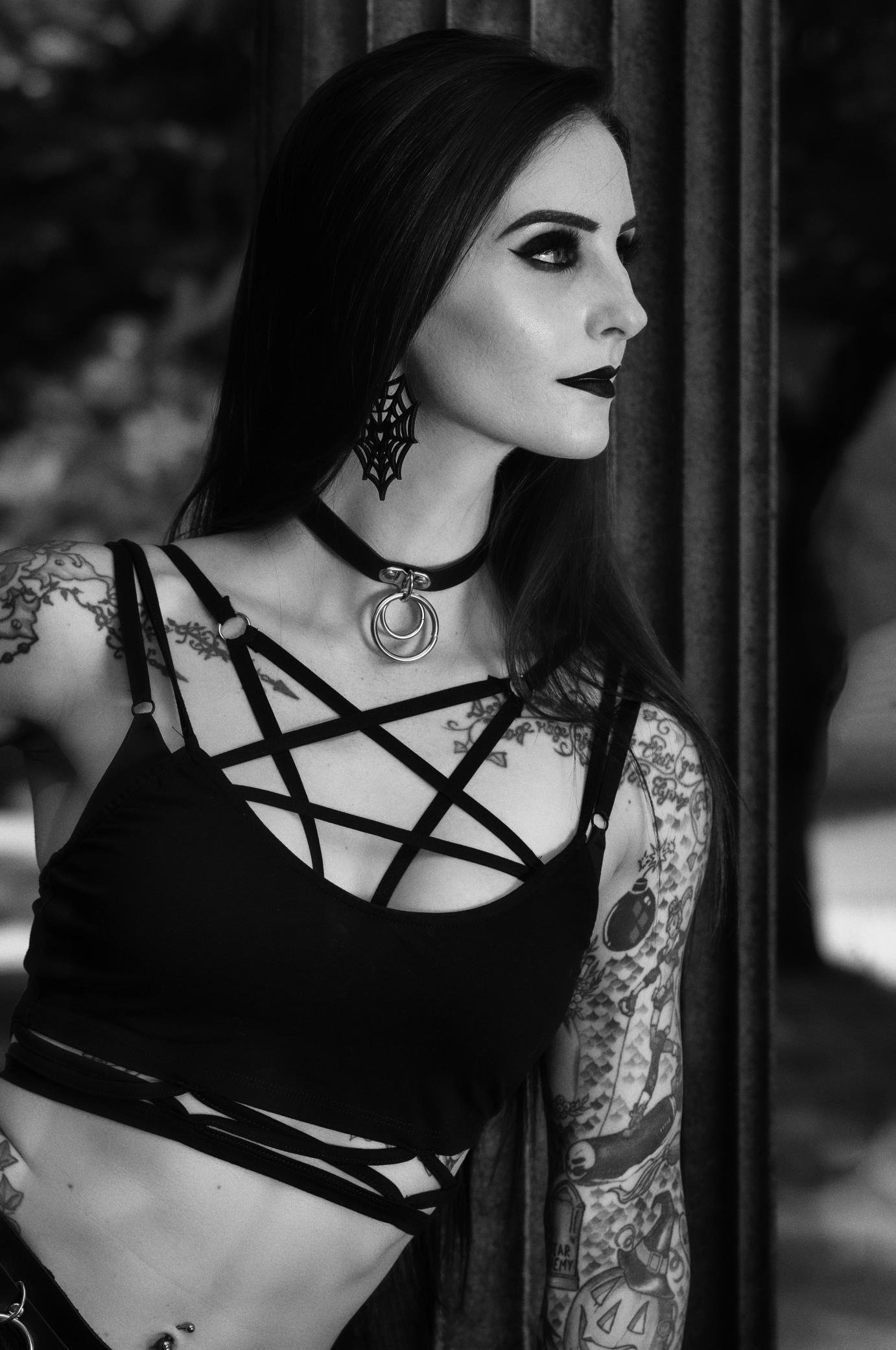 Tattooed gothic woman wearing a strappy black crop top with a choker and spiderweb earrings