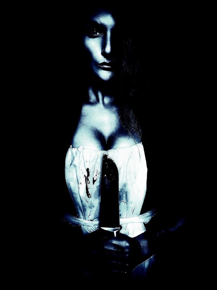 Woman in a white corset dress with blood stains, holding a large knife in dim lighting