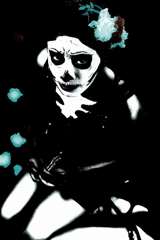 Woman with Dia de los Muertos skull makeup and flower crown sitting in a dark setting