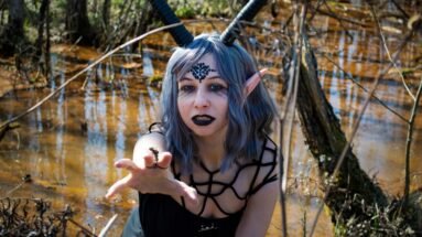 Gothic elf-like woman with horns and black lips reaching out in eerie swamp environment