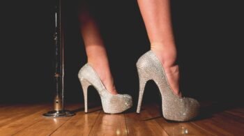 Extreme high heels with rhinestones next to a dance pole on wooden floor