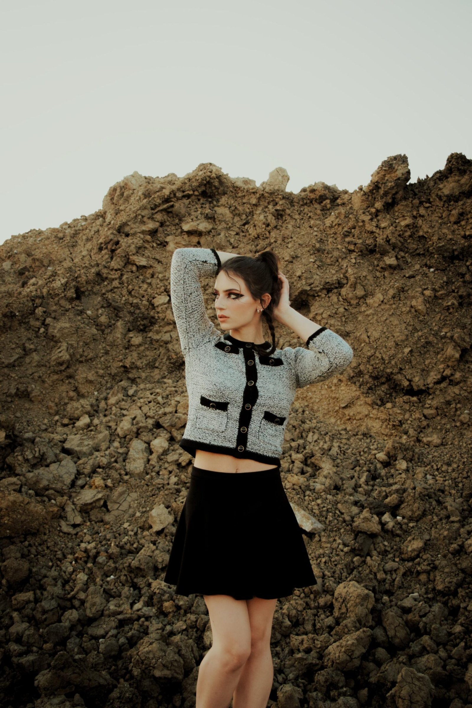 Woman posing against a rocky background in a high-waisted black skater skirt and cropped jacket
