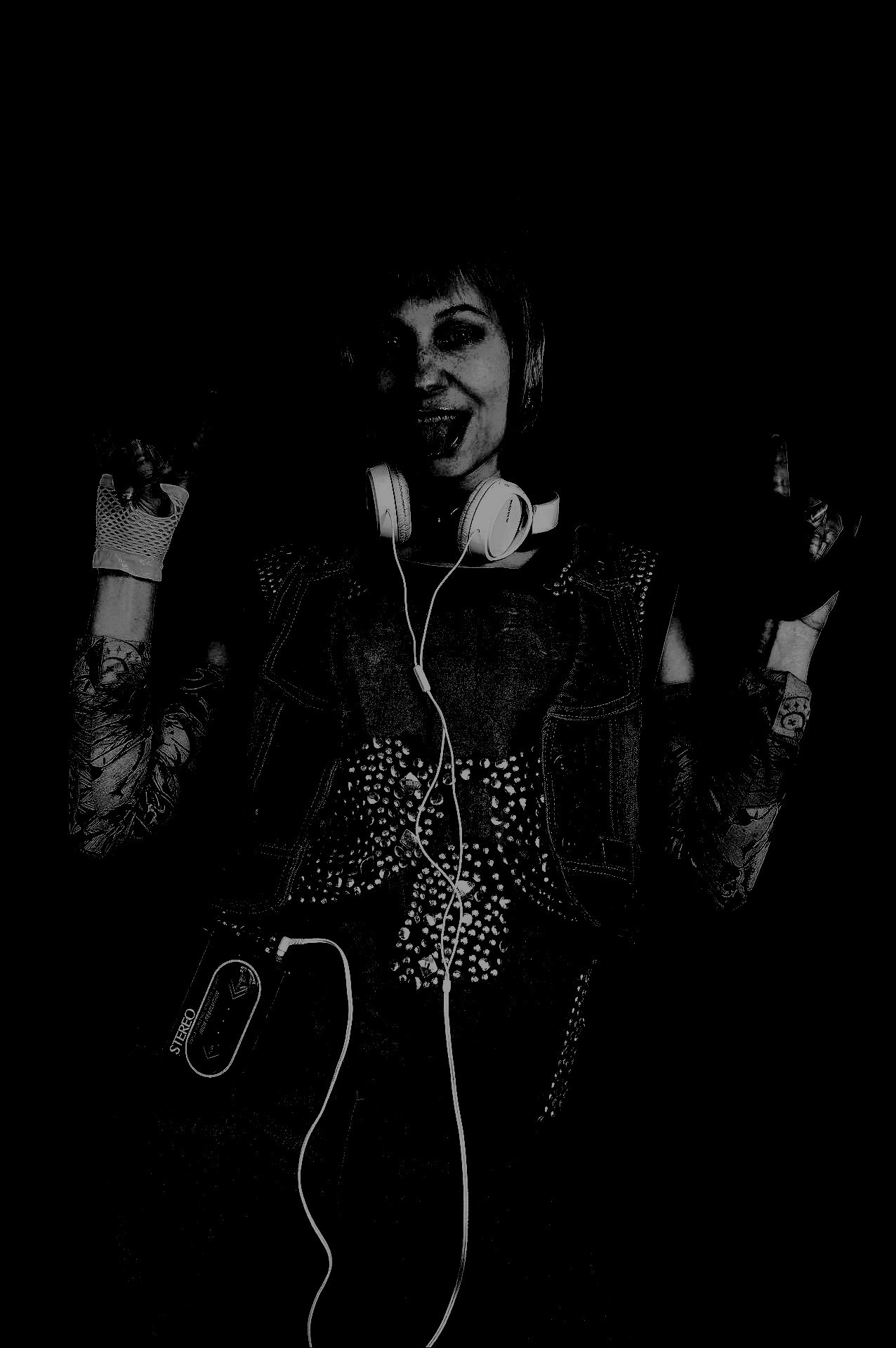 Female rocker in studded attire, headphones around her neck, striking a rebellious pose in the dark.