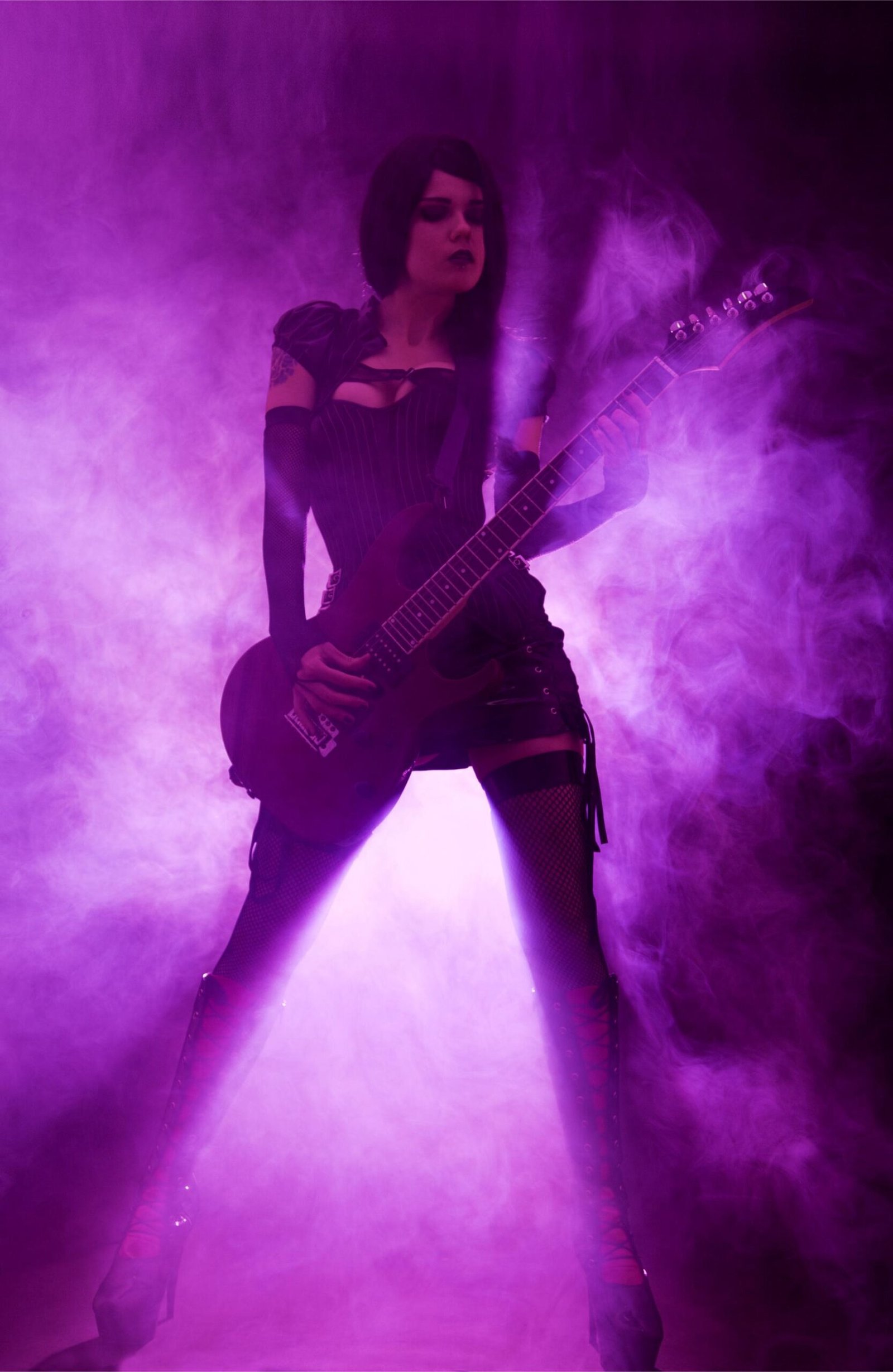 Gothic female guitarist in black corset, fishnets, and high boots playing guitar in violet smoke. 