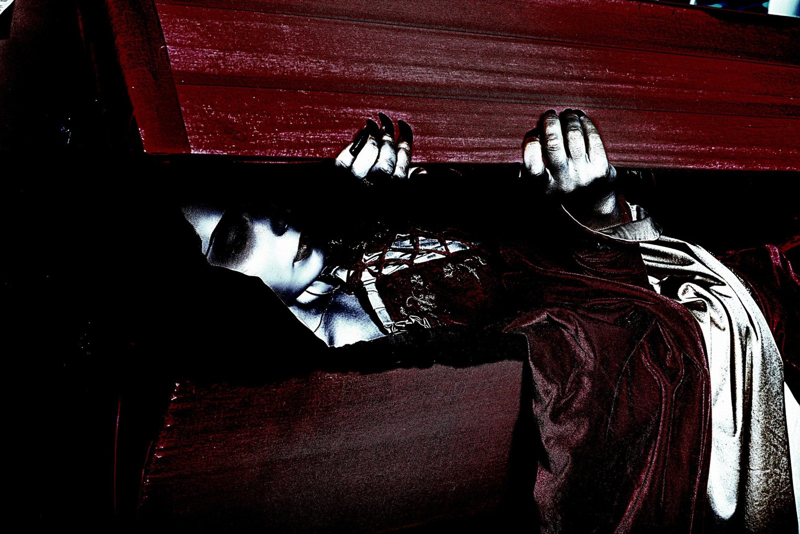 Pale gothic woman rising from a red wooden coffin wearing a dark corset dress