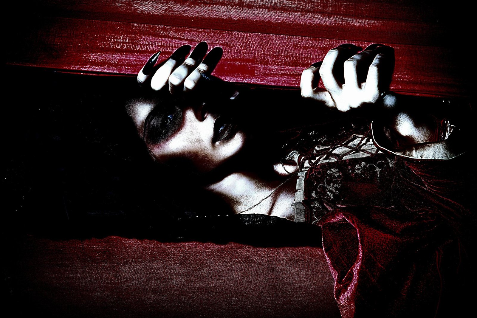 Close-up of vampire woman with dark makeup gripping the edge of a coffin lid