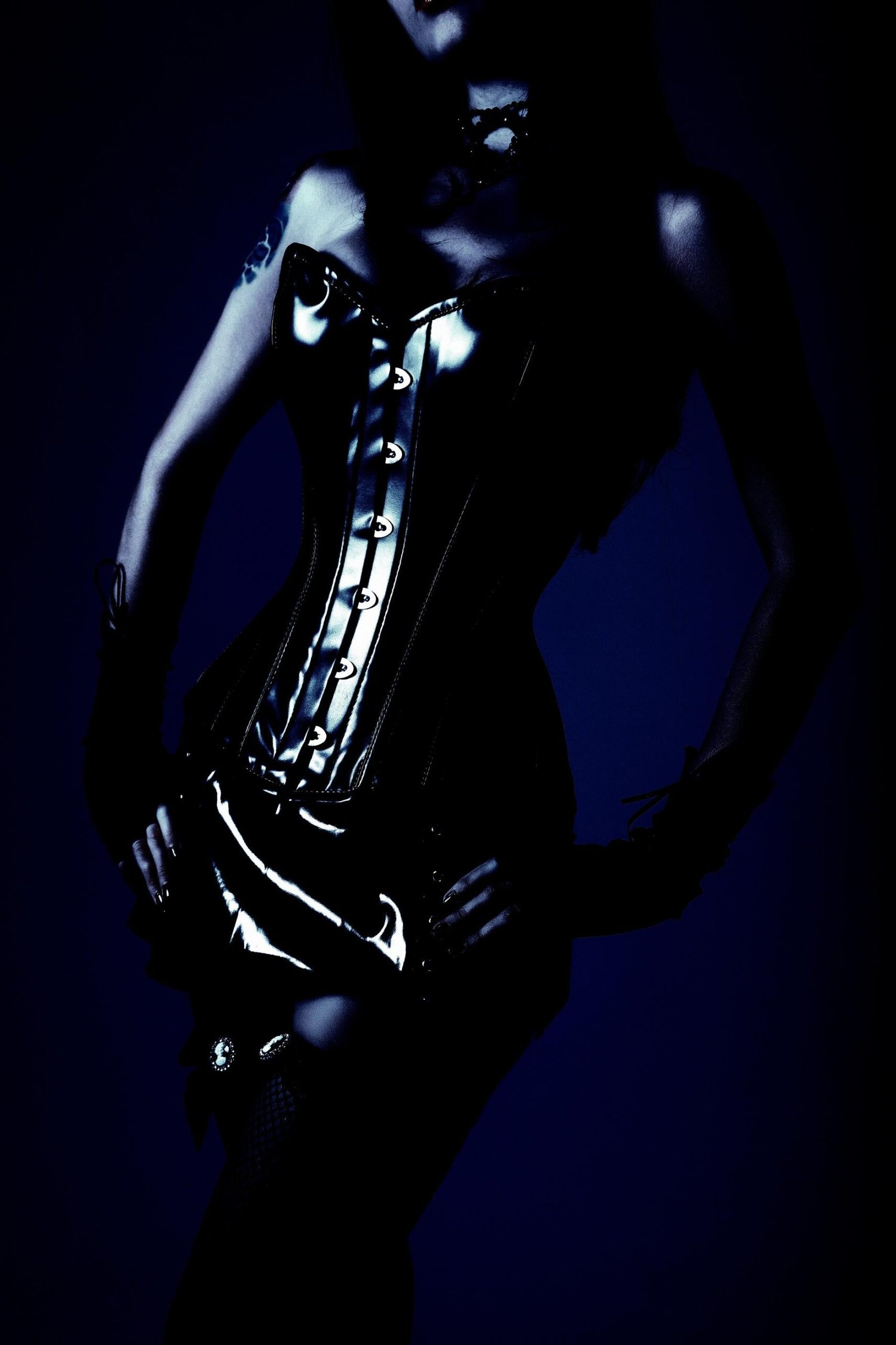 Woman in a black lace corset top and gloves posing in dramatic shadow lighting