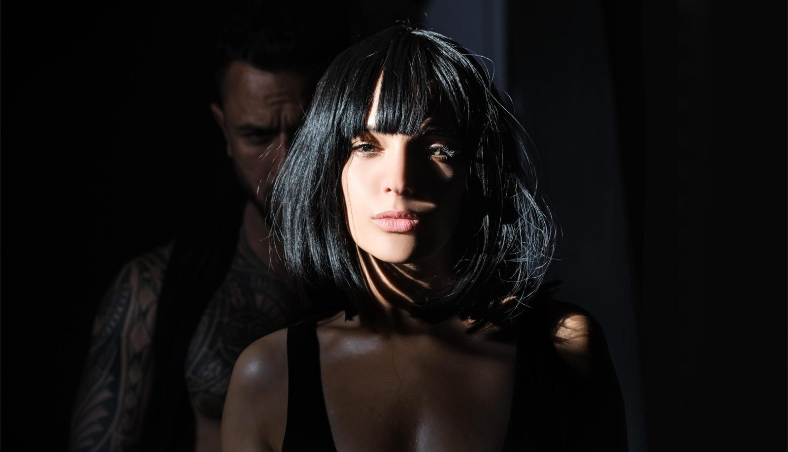 Woman with sharp black bob under spotlight, mystery and defiance