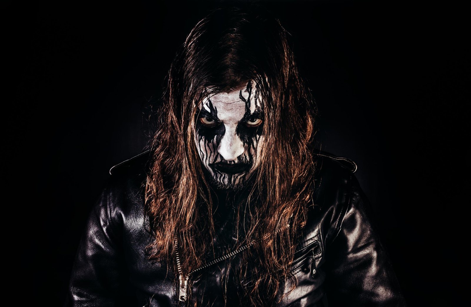 Black metal musician with corpse paint and leather, grim and intense stare