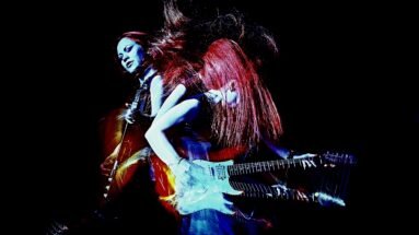 Double-exposure image of a woman playing electric guitar with vibrant red and blue lighting effects.
