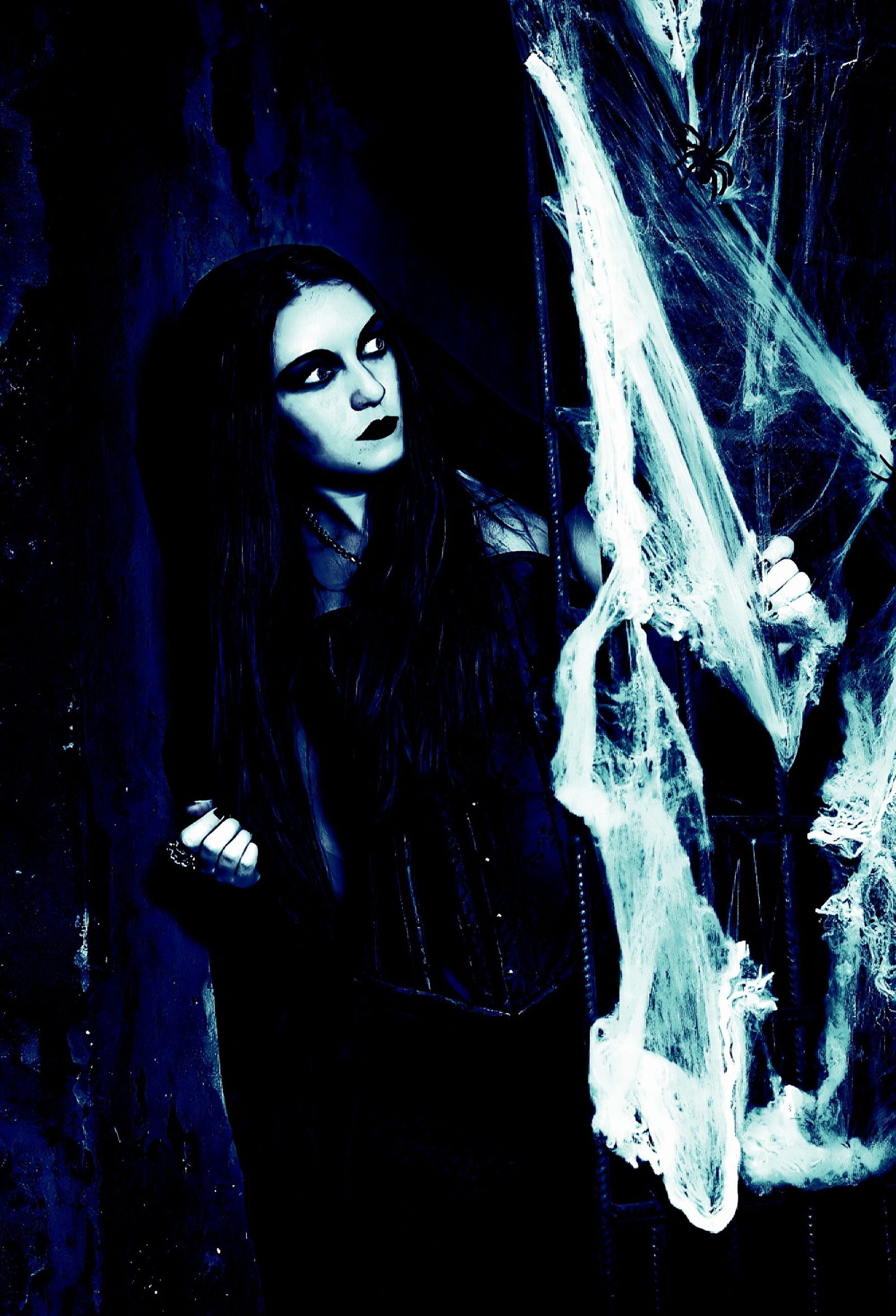 Gothic woman in black corset peering through cobwebs in a spooky, dark setting with heavy shadows.