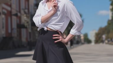 Woman in a black skater skirt and tied white shirt posing confidently in an urban setting