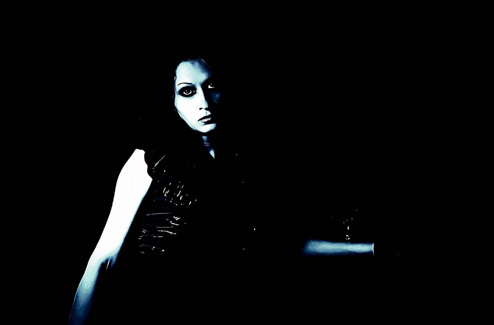 Pale goth woman in black latex corset, dark makeup, sitting in a moody, dimly lit environment.