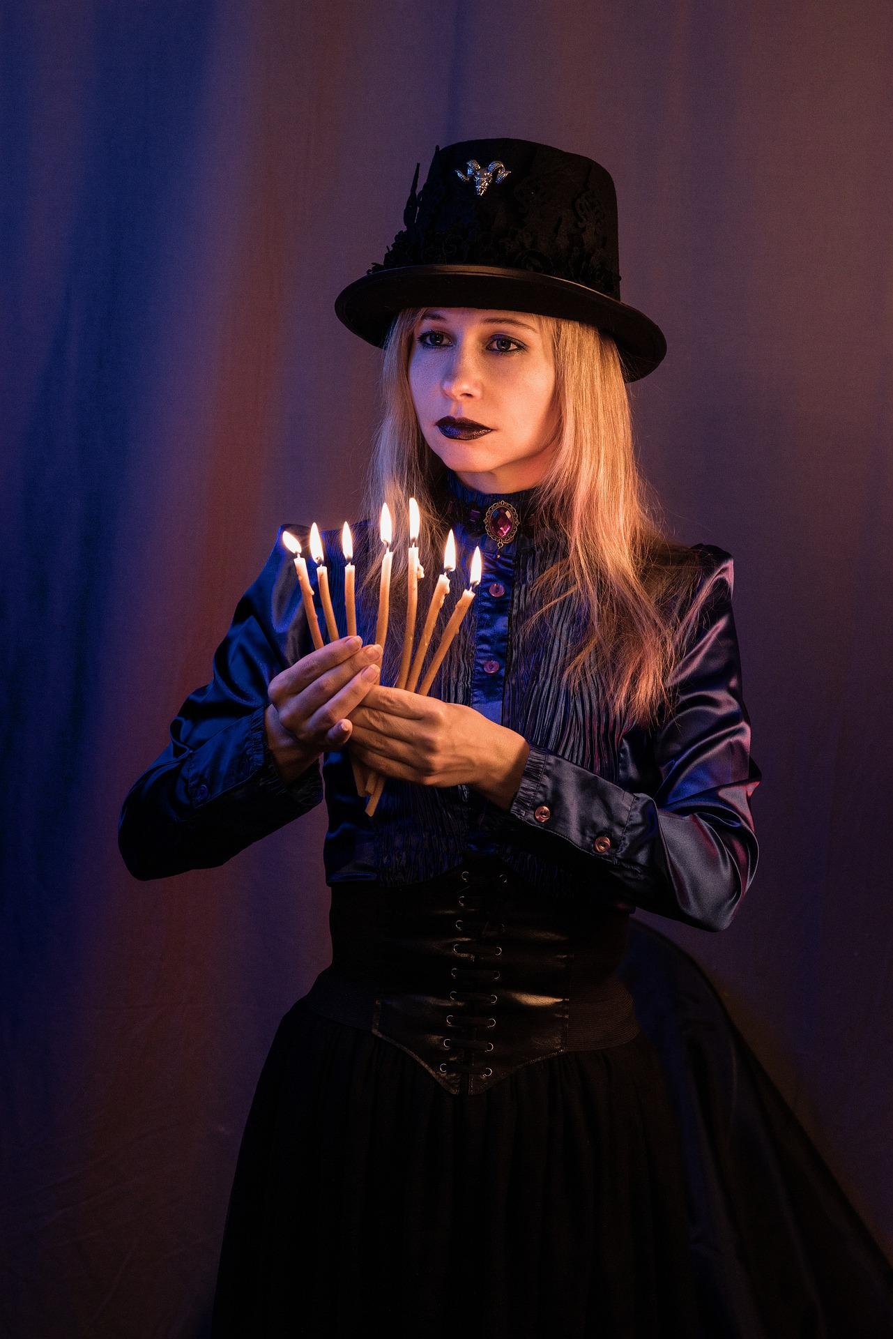Red-haired woman in black strappy bodysuit holding two crystal balls in front of red-black drapes. 