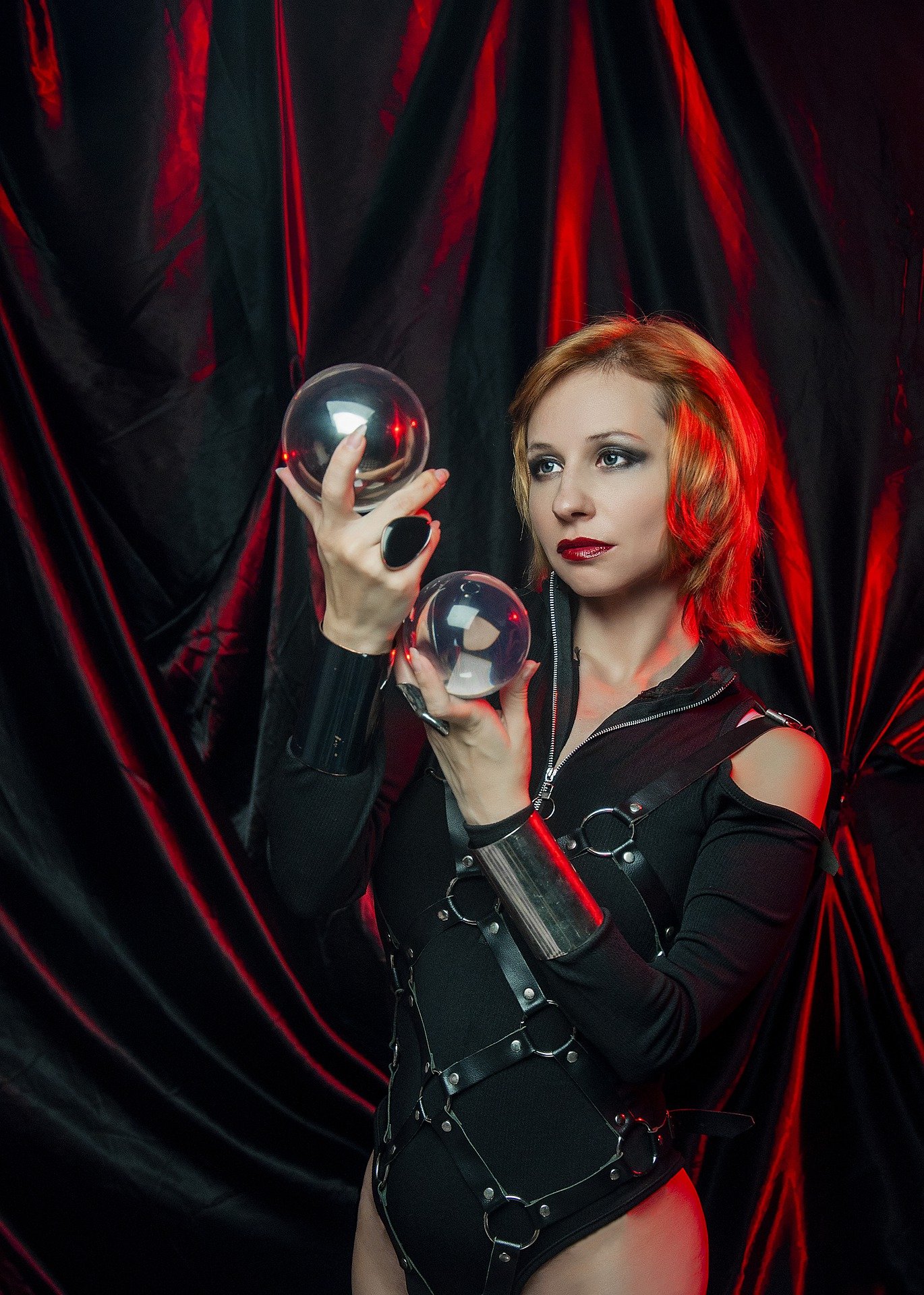 Blonde gothic woman in blue blouse and black corset holding lit candles, under moody low light. 