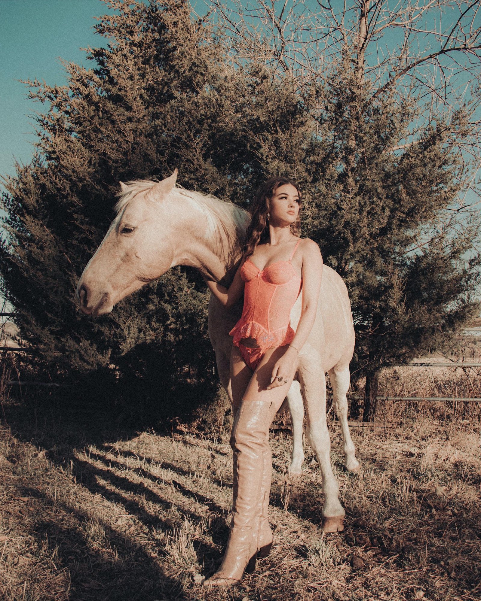Woman in pink corset and tan thigh-high boots standing beside white horse